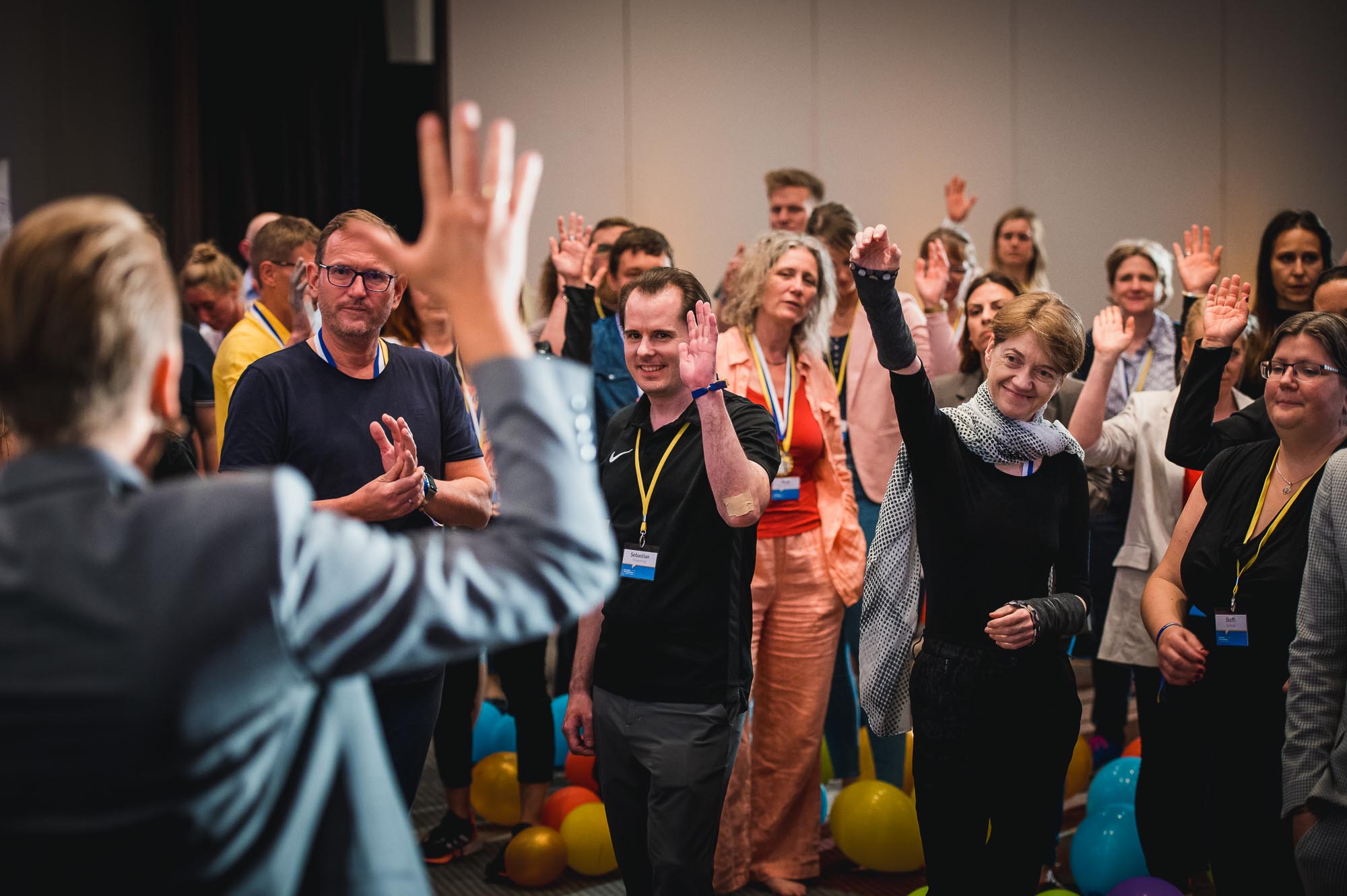 Teilnehmende eines Seminars heben die Hand. Vorne steht ein Tobias Beck